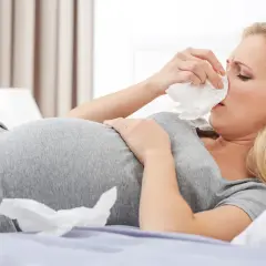 Schwangere Frau mit Schnupfen im Bett, die nach Hausmitteln gegen Mundrose sucht.