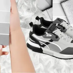 Dłonie trzymają paletę szarości, sugerując kolor roku 2026. Obok stylowe, szare buty sportowe na puszystym tle.
