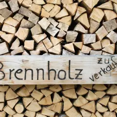 Holzstapel mit einem Schild "Brennholz zu verkaufen". Das Holz ist gespalten und bereit für den Winter, ob esche oder buche.