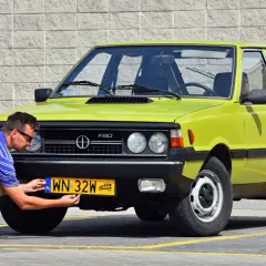 Mężczyzna przykręca żółtą tablicę rejestracyjną do zielonego Poloneza. Czy to auto ma już ile lat musi mieć auto na zabytek?