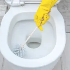Main jaune nettoyant le tartre WC avec une brosse.
