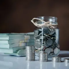 Stos banknotów i słoik pełen monet. Zastanawiasz się, jak zapłacić podatek od darowizny od obcej osoby?