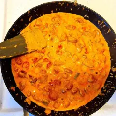 En stekpanna med krämig korv stroganoff bubblar. En spatel lyfter upp en bit av den läckra grytan.