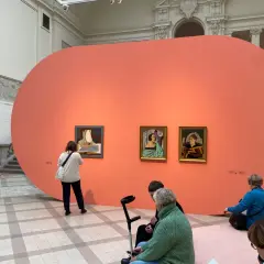 Wystawa prac Marii Nicz Borowiakowej. Zwiedzający oglądają obrazy na tle pomarańczowej ściany.