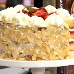 En vacker glutenfri jordgubbstårta täckt med vispgrädde och mandelspån, toppad med färska jordgubbar.