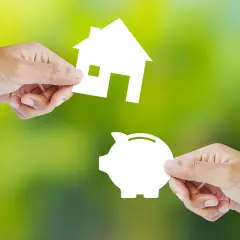 Manos intercambian una casa y una alcancía, simbolizando la decisión de alquilar o comprar.