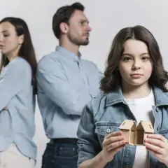 Smutna dziewczynka trzyma dwa domki, podczas gdy rodzice stoją odwróceni plecami. To obraz podstaw do odebrania dziecka matce.