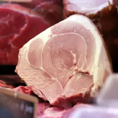 Gros plan sur une pièce de viande rose pâle, probablement une côte de porc, avec des marbrures de gras. Derrière, on aperçoit de la viande rouge vif.