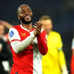 Uśmiechnięty Raheem Sterling w czerwono-białej koszulce, klaszczący. Jego statystyki w tym sezonie są imponujące.