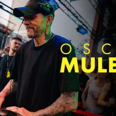 Oscar Mulero, DJ con cuffie e cappellino, mixa musica in un locale affollato. Il suo nome campeggia in giallo.