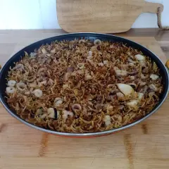 Fideos fideuá con calamares y gambas, listos para servir en una paellera.