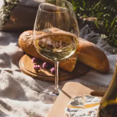 Un bicchiere di vino bianco, pane, formaggio e ciliegie su una coperta da picnic. Le caratteristiche del sangiovese vino sono perfette per un picnic.