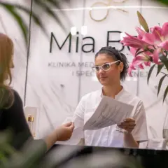 Recepcjonistka w klinice dermatologii estetycznej podaje dokument pacjentce.