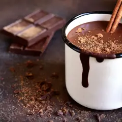 Cioccolata calda cremosa con cacao e cioccolato, guarnita con cannella e cacao in polvere. Accanto, pezzi di cioccolato fondente e spezie.