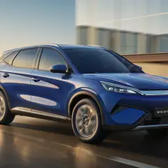 BYD Atto 3 blu in movimento, con la sua notevole autonomia, sfreccia su una strada urbana al tramonto.