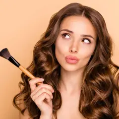 Ragazza con pennello da trucco, pensierosa, mentre impara a truccarsi.