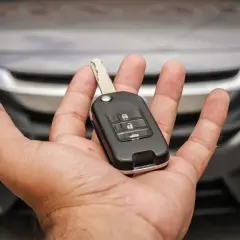 Mano che tiene una chiave auto moderna, pronta per duplicare la chiave auto. Auto scura sullo sfondo.