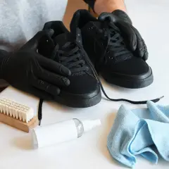 Manos enguantadas limpian zapatos negros con cepillo y spray.