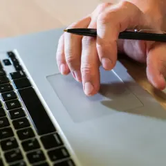 Mano con bolígrafo sobre el touchpad de un portátil, como si buscara qué es un hash.