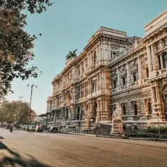 Edificio imponente su via dei Cosmati, con auto che transitano e un albero ombroso.
