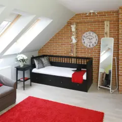 Stylowe lustro do pokoju młodzieżowego, stojące obok czarnej kanapy i ceglanej ściany.