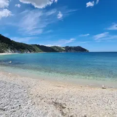 Spiaggia di Portonovo con il Monte Conero sullo sfondo. Acqua cristallina e cielo azzurro.