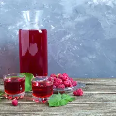 Karafka i kieliszki wypełnione rubinową nalewką z malin na spirytusie. Obok świeże maliny i listki.