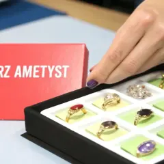 Dłoń wybiera pierścionek z ametystem. Na czerwonym tle napis "Wybierz ametyst".