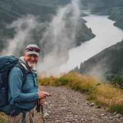 Uśmiechnięty turysta z plecakiem na tle mglistej doliny. Może śpiewa pieśni pielgrzymkowe, idąc szlakiem.