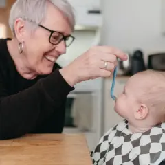 Glad mormor matar bebis med smakportioner. Första maten för en 4 månader gammal bebis.