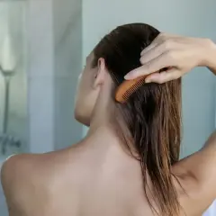 Une femme se peigne les cheveux mouillés, préoccupée par la **chute de cheveux** causée par l'**eau calcaire**.