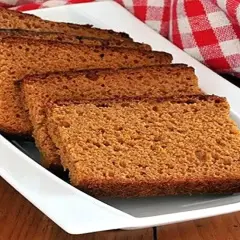 Tranches de pain d'épices moelleux disposées sur un plat blanc, avec un torchon à carreaux rouges en arrière-plan.