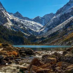 Majestuosas montañas nevadas flanquean el sereno lac de Gaube, con un arroyo rocoso que desemboca en sus aguas turquesas.