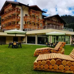 Hotel Dolomia Soraga: un'oasi di relax con vista sulle montagne. Panchine in legno e prato verde invitano al riposo.