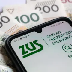 Pracujący emeryt sprawdza na telefonie aplikację ZUS, analizując przeliczenie emerytury na tle polskich banknotów.