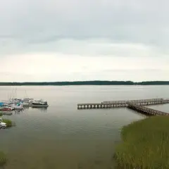 Widok na jezioro, gdzie wypływa roś. Widać pomosty, łodzie, pływające domki i plażę.