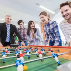 Colleagues laugh and play foosball, showcasing great employee engagement games.