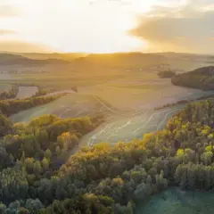 Zachód słońca nad pagórkami, gdzie przebiega szlak wygasłych wulkanów. Złote światło oświetla lasy i pola.