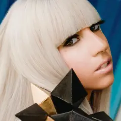 Lady Gaga, con capelli biondo platino e un look audace, cattura l'essenza del suo **inizio carriera** con un'espressione intensa e un accessorio geometrico.