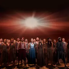 Chór w "Aidzie" w Teatrze Roma, spektakl trwa. Grupa ludzi w strojach z epoki na tle dramatycznego, rozświetlonego nieba.