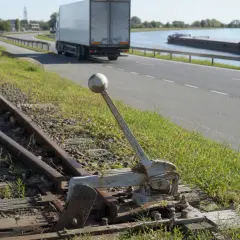 Alte Weiche neben Gleisen. Ein LKW und ein Frachtschiff sind auf der Straße und dem Wasser zu sehen, verschiedene Verkehrsmittel.