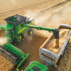 Zielona maszyna rolnicza podczas żniw wysypuje zboże do przyczepy.