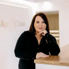 Kobieta w czarnej bluzce opiera się o ladę w klinice AntiAge Clinic.