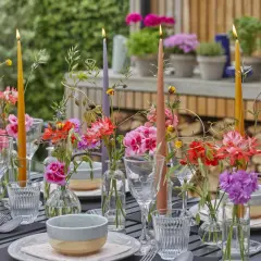 Tavola apparecchiata con candele colorate e fiori freschi, un'ispirazione per decorazioni estive fai da te.