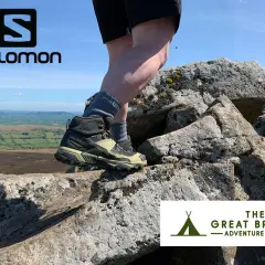 Stopy w butach Salomon X Ultra 5 Mid GTX na skalistym szlaku, z widokiem na zielone wzgórza.