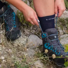 Hands tying the laces of a dark grey hiking boot with teal accents. Learn how to wear hiking boots for your next adventure.