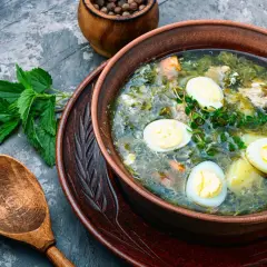 Zupa szczawiowa przepis babci. Aromatyczna, zielona zupa z jajkiem i ziemniakami, podana w glinianej misce z drewnianą łyżką.