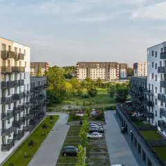 Nowoczesne osiedle mieszkaniowe, z białymi blokami i balkonami, otoczone zielenią. W tle widać kolejne budynki, tworzące krajobraz jak z **okam capital**.