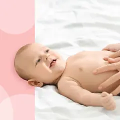 Uśmiechnięte dziecko na białym tle, ręce masują brzuszek, łagodząc dyschezję.