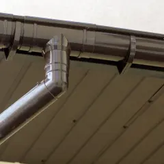Brązowe mocowanie rynny z tworzywa sztucznego, połączone z rurą spustową, zamontowane na dachu.